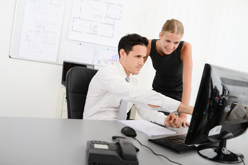 two young business people in office meeting and looking at data in computer