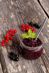 berry jam in a glass jar and fresh red currants on wooden board,