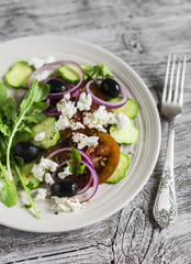 Greek salad - salad with tomatoes, cucumbers, olives and feta cheese on a white plate on a light wooden background