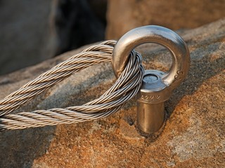 Detail of steel bolt anchor eye in rock. The end knot  of steel rope. Climbers path in rocks via...