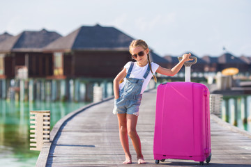 Little adorable girl with big luggage near water villa