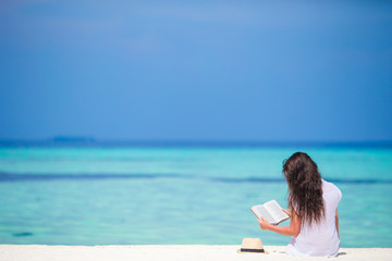 Fototapeta premium Young woman reading book during tropical white beach