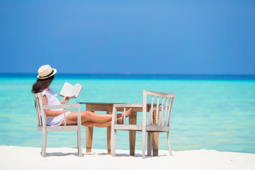 Fototapeta na wymiar Young woman reading at outdoor beach cafe