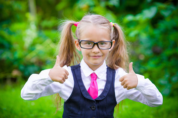 Fototapeta na wymiar Little happy girl showing thumbs up. Back to school outdoor