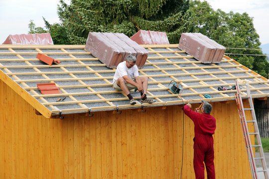 Zwei Männer beim Dachdecken eines Holzhauses