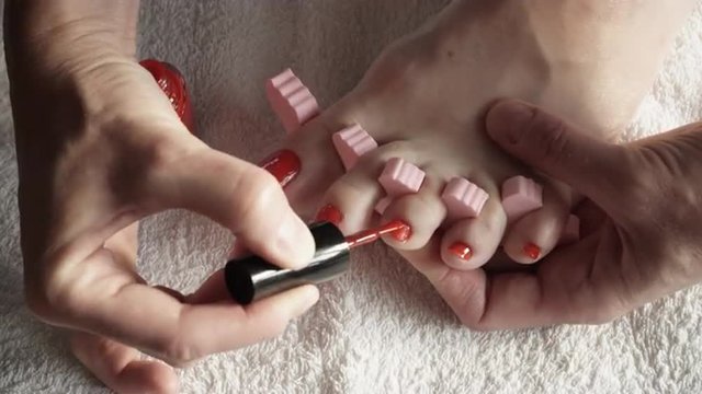 Closeup woman painting nails of her feet, applying red toenails. 4K