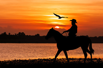 silhouette of Cowboy sitting on his horse at river sunset backgr