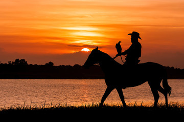 silhouette of Cowboy sitting on his horse at river sunset backgr