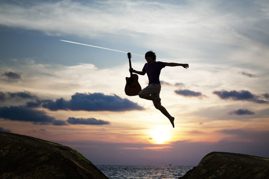 silhouette of brave guy holding the guitar jumping  through the gap，inspiration and success concept.
