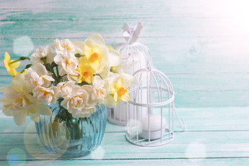 Bright  narcissus flowers in blue vase and candles in ray of light  on turquoise painted wooden planks. Selective focus. Place for text..
