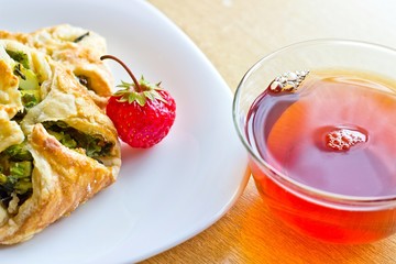 Fresh baked homemade puff pastry cakes, strawberry with fresh strong black tea in glass cup