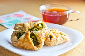 Fresh baked homemade puff pastry cakes with fresh strong black tea in glass cup. Selective focus on cake