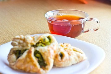 Fresh baked homemade puff pastry cakes with fresh strong black tea in glass cup. Selective focus on cup