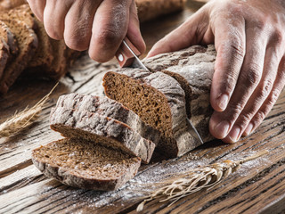 Man's hands cutting bread on the wooden plank.