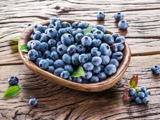 Ripe blueberries in the bowl on the wooden table.