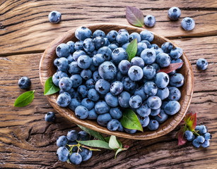 Ripe blueberries in the bowl on the wooden table.