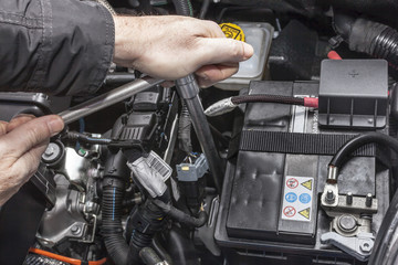 Mani che serrano la batteria nel motore di un'automobile con una chiave