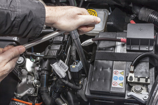 Mani che serrano la batteria nel motore di un'automobile con una chiave