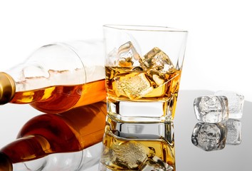 glass of whiskey near bottle and ice cubes on black table with reflection