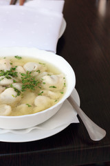 Bowl of broth with small meat dumplings and chives.