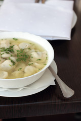 Bowl of broth with small meat dumplings and chives.