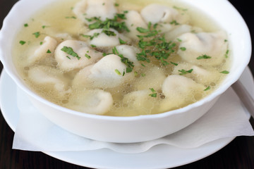 Bowl of broth with small meat dumplings and chives.