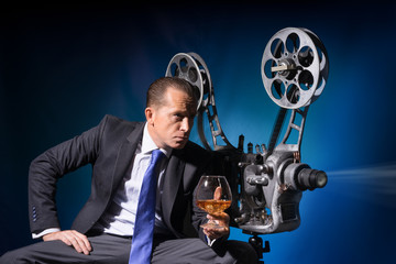 A man with a glass of cognac looking through vintage film projector
