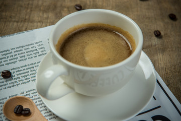 White cup of Espresso with Newspaper on the wooden table in the