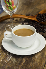 Coffee mug made of white ceramic wafer sticks and coffee beans in a wooden spoon on a wooden floor.