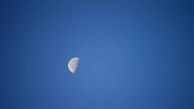 Moon moves across cloudless blue sky