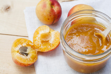 Homemade apricot jam and fresh apricots with leaves on the wooden table