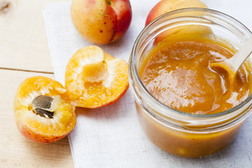 Homemade apricot jam and fresh apricots with leaves on the wooden table