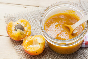 Homemade apricot jam and fresh apricots with leaves on the wooden table