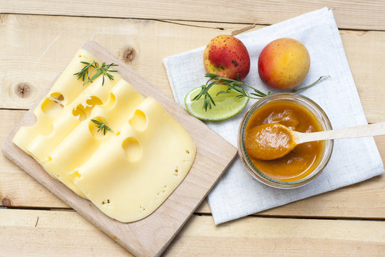 Maasdam several slices of cheese on wooden board, homemade apricot jam and fresh apricots 