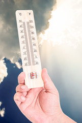 Hand holding thermometer on blue sky background