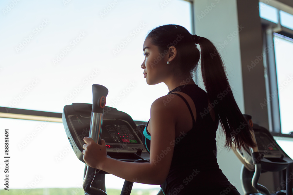 Wall mural silhouette of attractive young woman at the gym exercising on the xtrainer machine