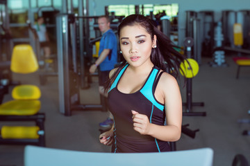 Fototapeta na wymiar Attractive asian girl running on the treadmill in the gym. Left profile face shot