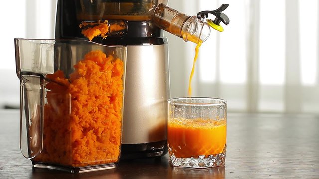 Fresh carrot juice pours of juicers in a glass on the table.