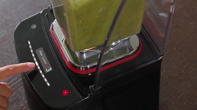 Female hand exposes the the mode to the blender. Green cocktail pours in glass.