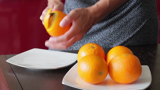 Ripe tasty oranges with peel. Close-up  young housewife removing orange peel.
