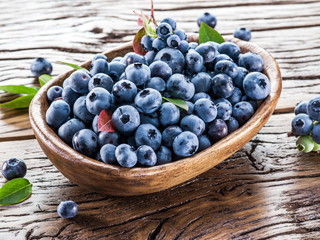 Ripe blueberries in the bowl on the wooden table.