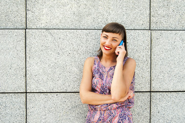 Young woman talking on phone by the wall in city smiling.