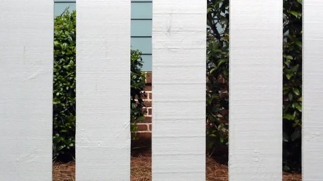 A sliding view of a suburban home through a white picket fence