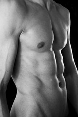 Fototapeta na wymiar The torso of a lean but muscular young man. In black and white. Black studio background.
