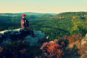 Hiker in black with red baseball cap on sharp  cliff and watch to valley. Colorful summer day.