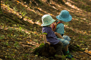 boy and girl with sunhats sitting on an old log in the autumn forest 