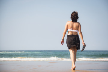 Girl walking towards the sea with flip flops in her hands on the beach in Ponta Do Ouro in Mozambique
