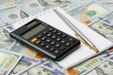 Calculator, pen and notepad on dollars