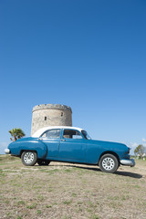 Classic vintage car in ocean blue parked in front of stone tower on a hill in Varadero, Cuba