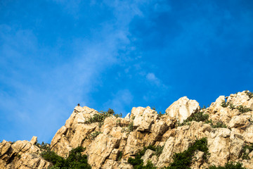 Stone or rock mountain with tree covering, blue sky and clounds